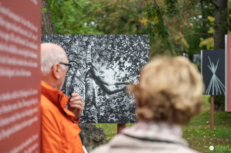 Lois Lammerhuber and Visitor Examining Black-and-White Photography Exhibit Outdoors