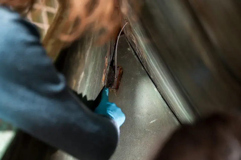 A conservator wearing blue gloves carefully applies material along the seam where copper sheeting meets the wooden frame structure of Poldi, the historic 10-meter whale sculpture at Wien Museum in Vienna, during the 'Tage der Restaurierung' (Restoration Days) public demonstration. The close-up perspective reveals the intricate junction between the metal skin and internal framework, showcasing the specialized conservation techniques required to maintain this beloved Prater landmark. The Tage der Restaurierung program provides visitors with hands-on insight into artwork preservation methods used at Vienna's museums.