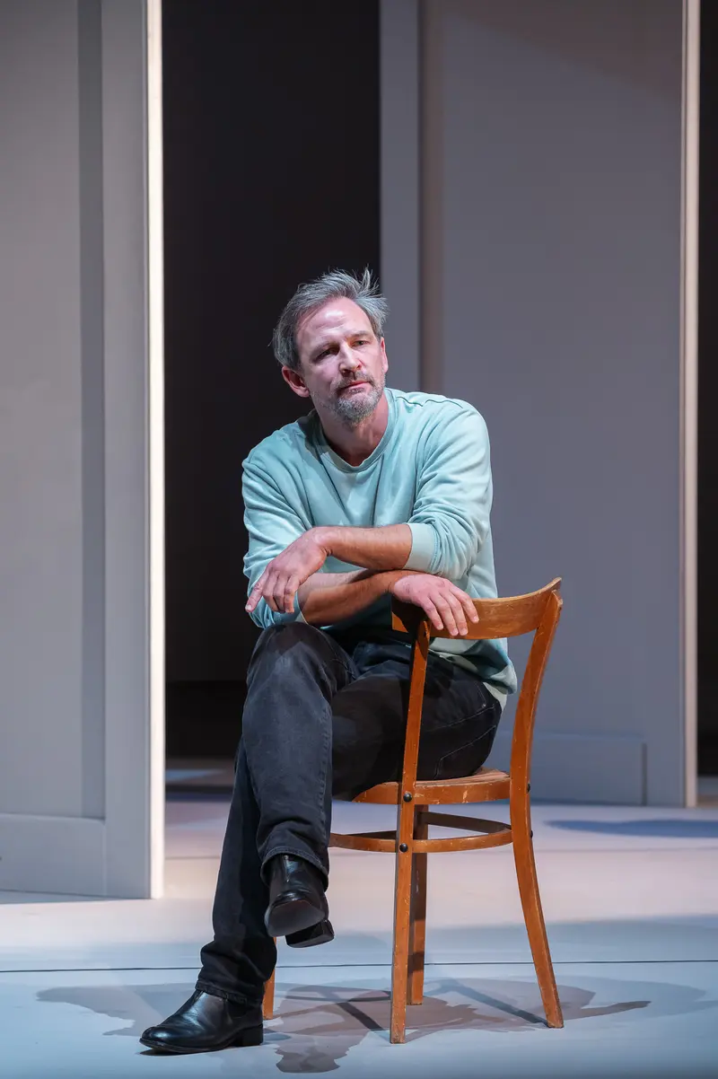 Contemplative Actor in Blue Shirt Seated on Wooden Chair at Kammerspielen