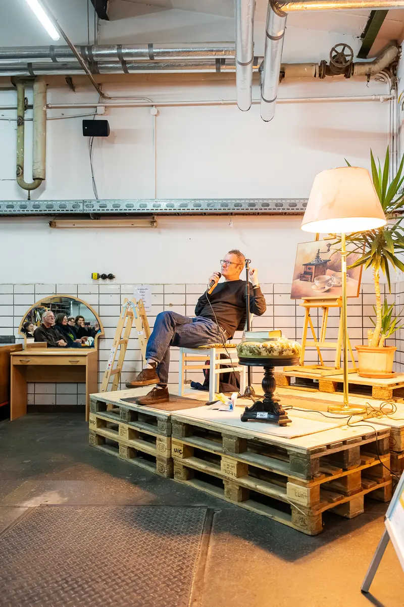 Relaxed Author Sitting on Wooden Pallets in Creative Workshop Space