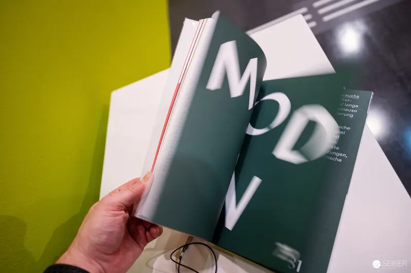 Wien Museum 'MIXED' Ausstellungseröffnung. Hand Holding Open Exhibition Catalogue Displaying Typography Against Yellow Gallery Wall