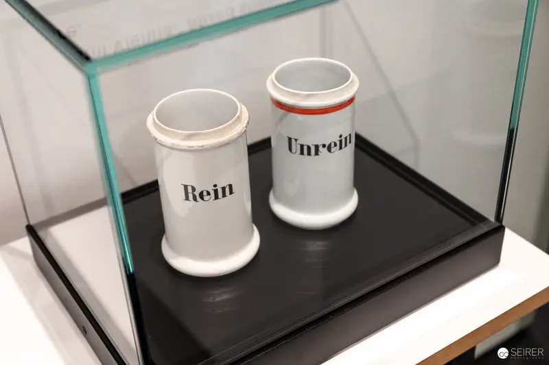 Wien Museum 'MIXED' Ausstellungseröffnung. Porcelain apothecary jars labeled "Rein" and "Unrein" in glass display case