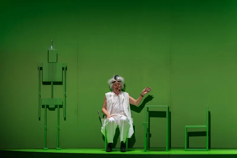 Actor in White Performing on Minimalist Green Stage at Josefstadt Theater