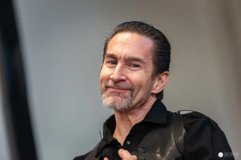 Middle-Aged Man in Black Jacket Smiling at Photography Event