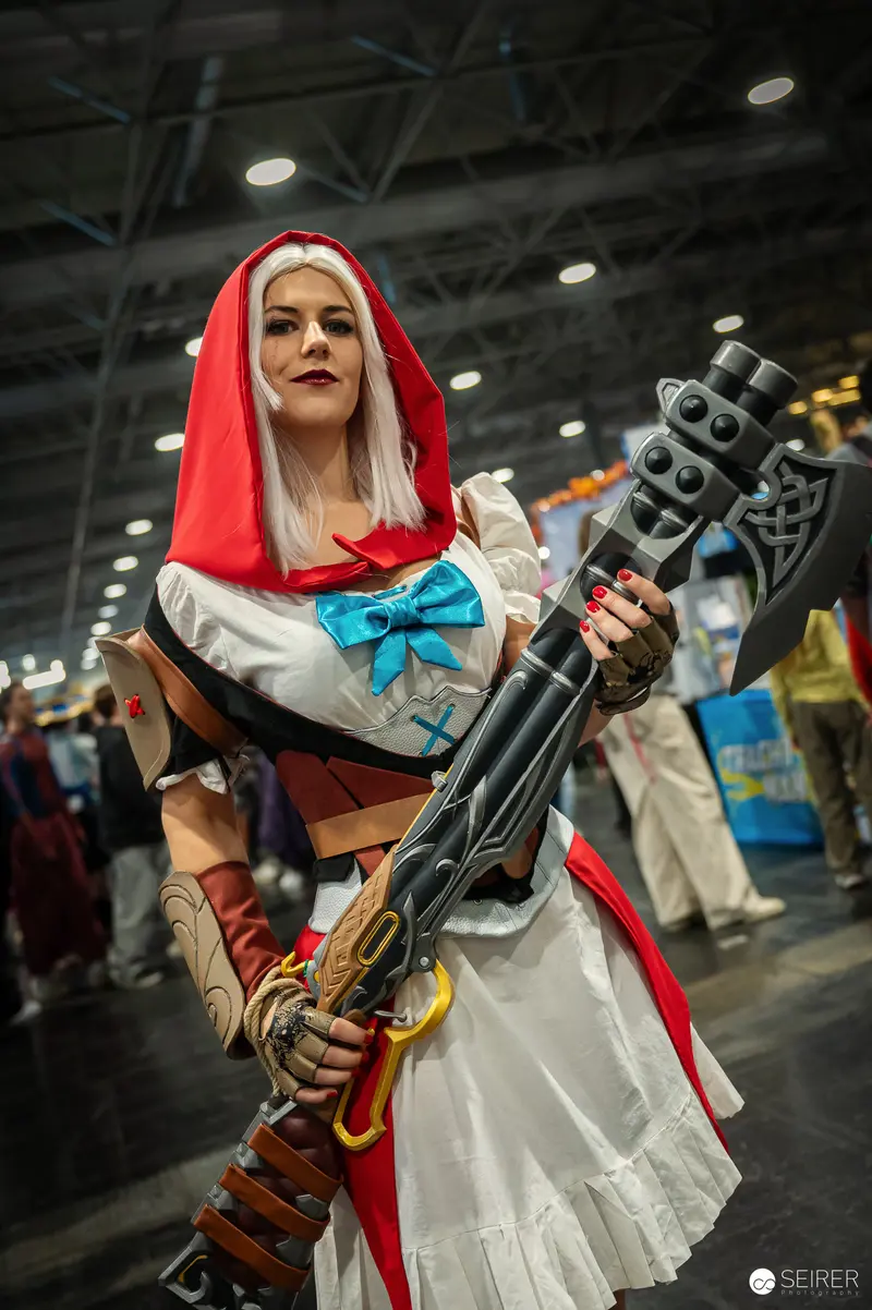 Cosplayer in Red Hood Wielding Steampunk Weapon at Comic Convention