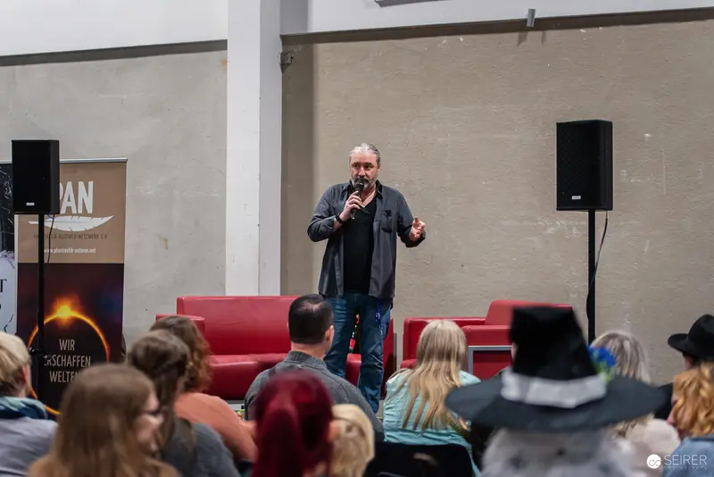 Speaker Presenting at Literary Event with Red Seating and Sound Equipment