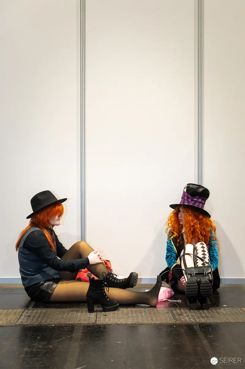 Two Cosplayers at Vienna ComicCon 2024 in Matching Curly Wigs and Hats