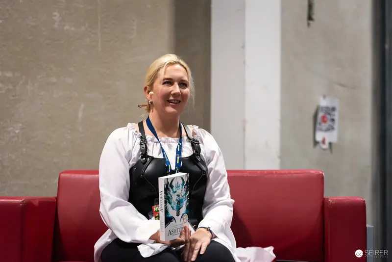 Cosplayer at Vienna ComicCon 2024 Showcasing Book and Enthusiastic Smile