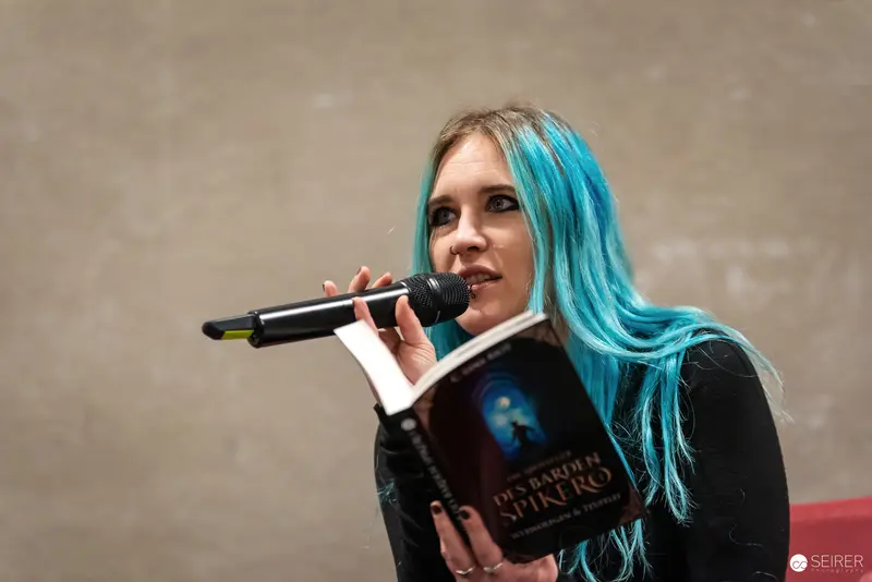 Blue-Haired Performer Reading Book on Stage at Vienna ComicCon 2024