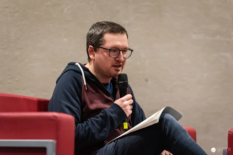 Speaker at Vienna ComicCon 2024 Discusses with Microphone and Open Book