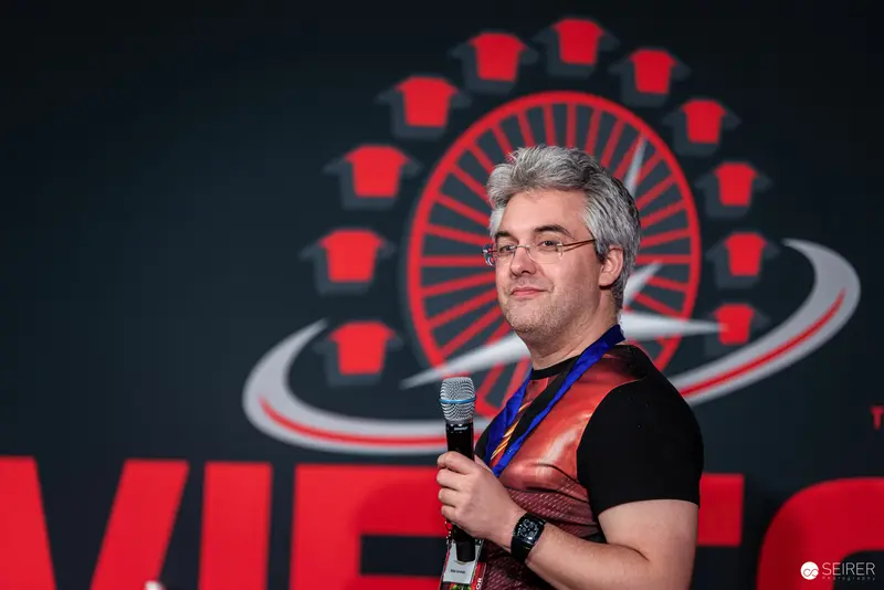 Speaker at Vienna ComicCon 2024 Presenting with Microphone Against Branded Background