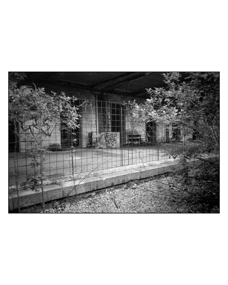 Graffiti-tagged abandoned railway platform behind wire fence, Villach–Grado route, 2024