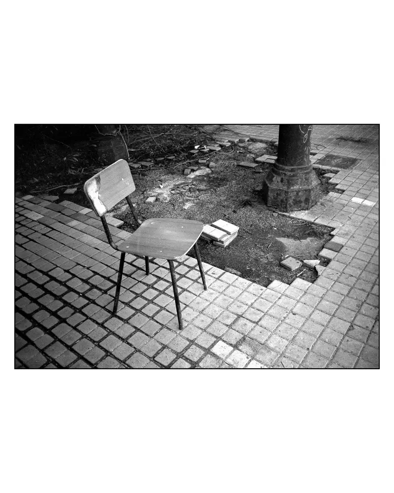 Abandoned wooden chair on cobblestone pavement beside cast-iron lamp post, Grado, 2024