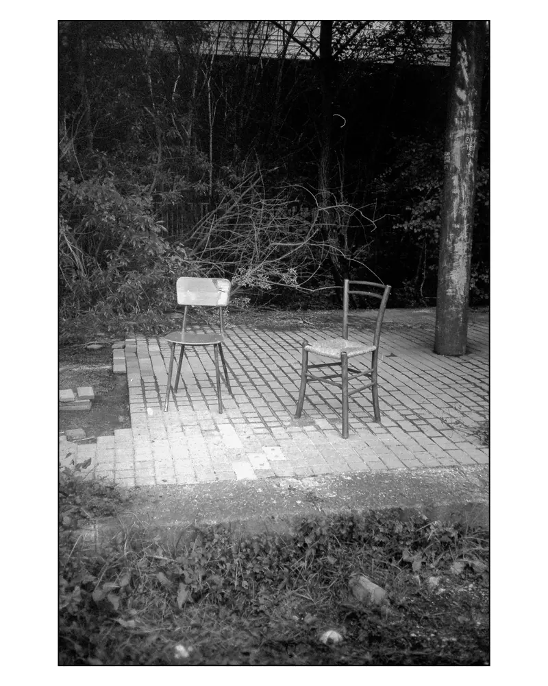 Two empty chairs on a brick terrace beside bare trees, Villach–Grado route, 2024