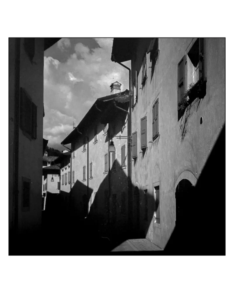 Narrow alley with shuttered facades and wall-mounted lamp on Villach–Grado route, 2024