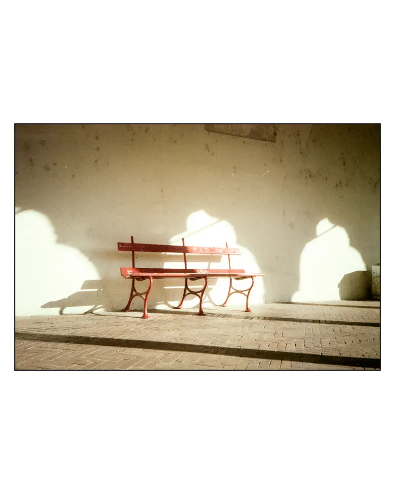 Empty red cast-iron bench against whitewashed wall, Grado, Italy