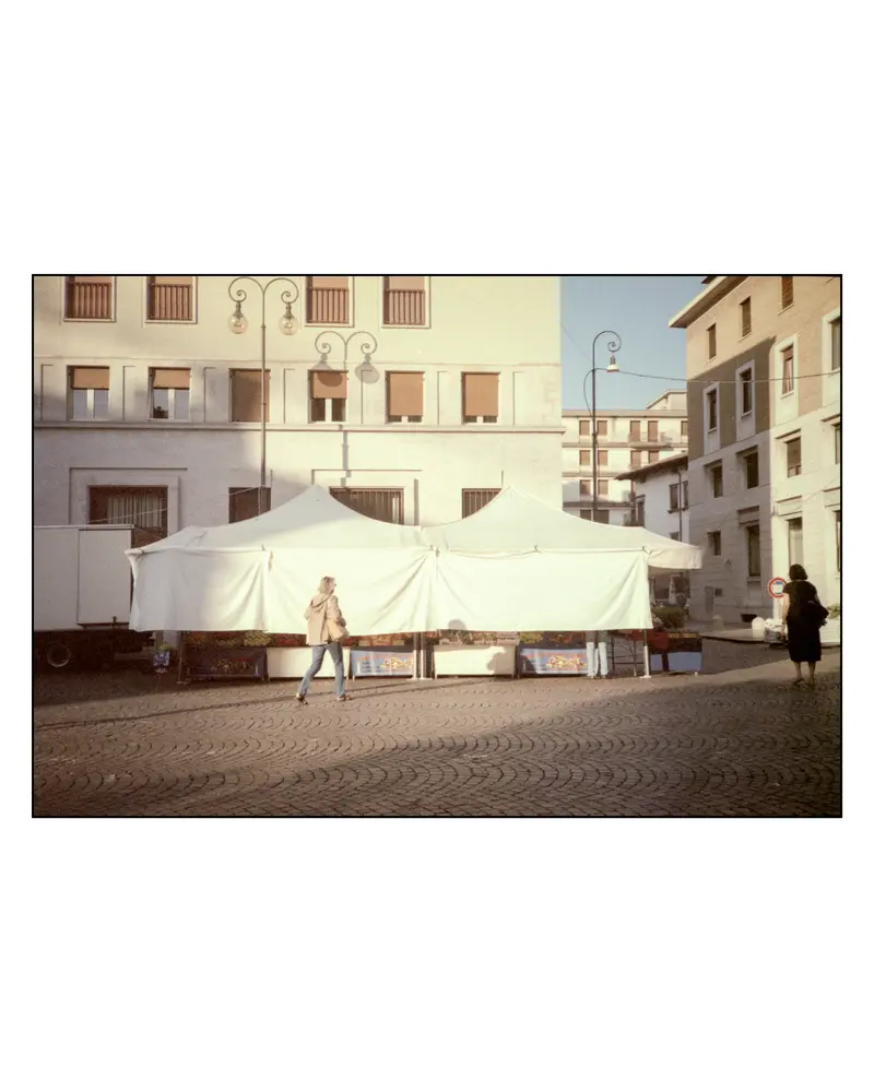 Pedestrians Passing Closed White Market Tents on Grado Cobblestone Square