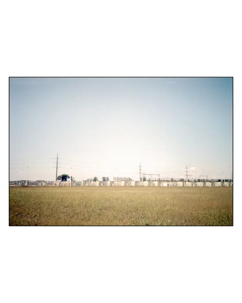Electrical substation and pylons behind dry grassland on the Villach–Grado route, 2023