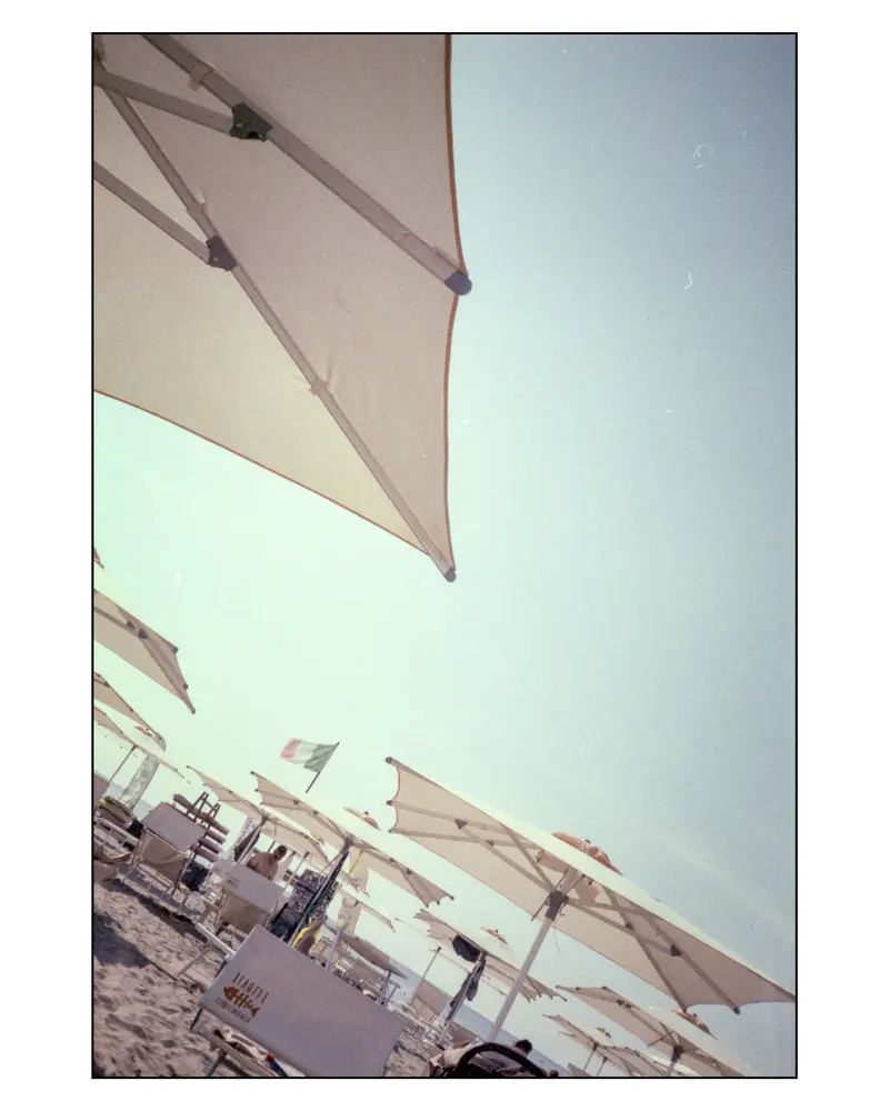 Rows of cream beach umbrellas and Italian flag on Grado's Adriatic sand, 2023