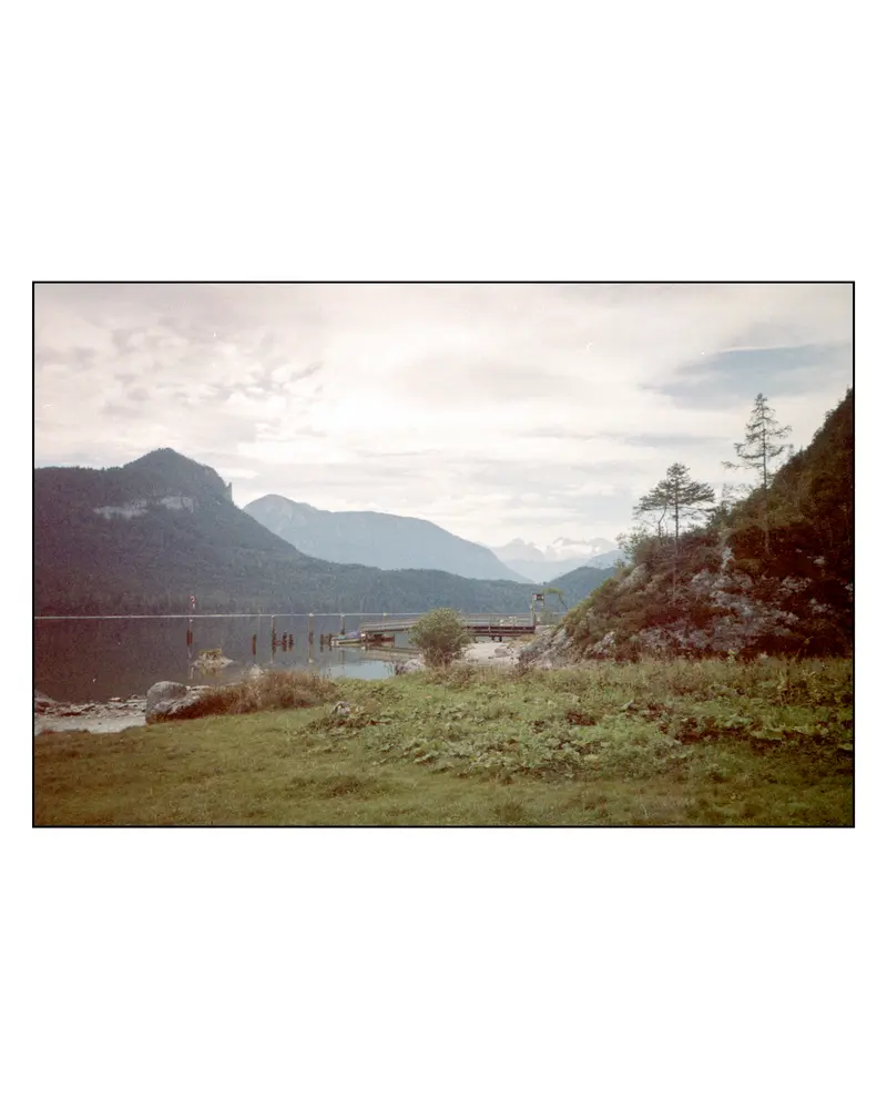 Alpine lake shoreline with wooden jetty and mountain ridges under overcast sky