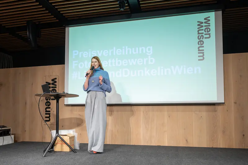 Woman Presenting at Design Week Awards Ceremony in Blue and Gray Outfit