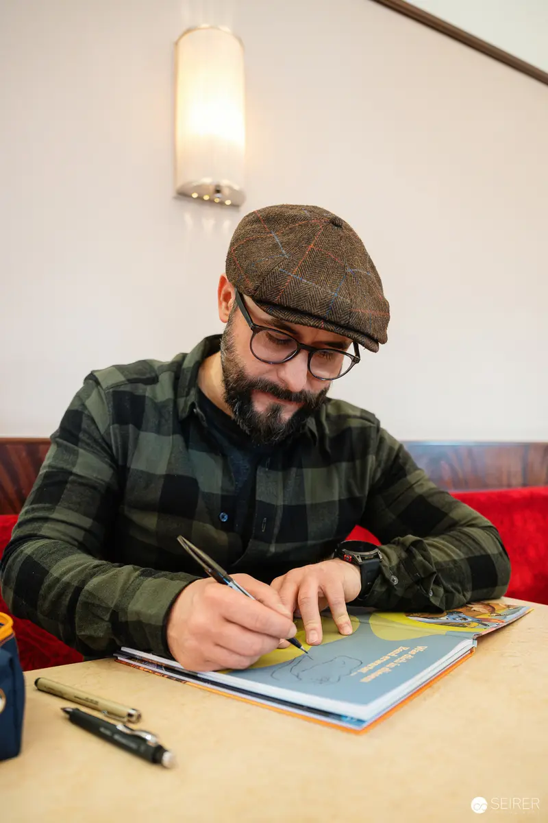 Author in Plaid Jacket and Flat Cap Writing at Cafe Table