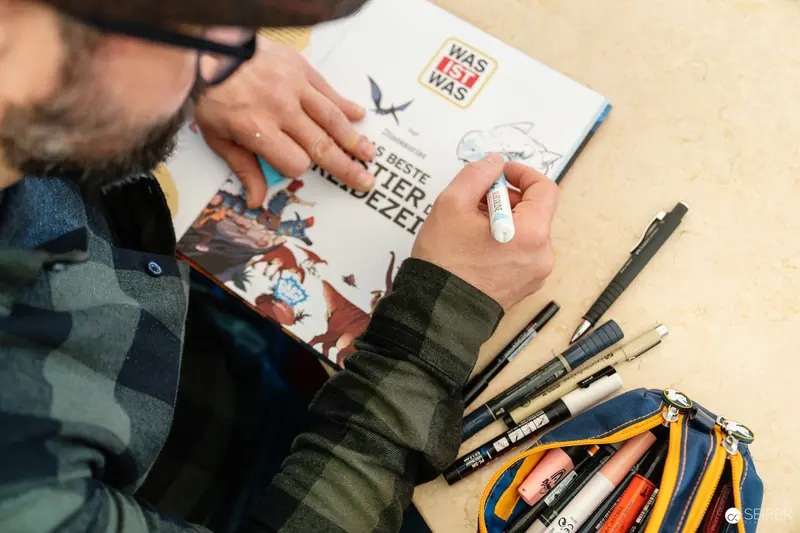 Artist Sketching in Detailed Illustration Book with Markers