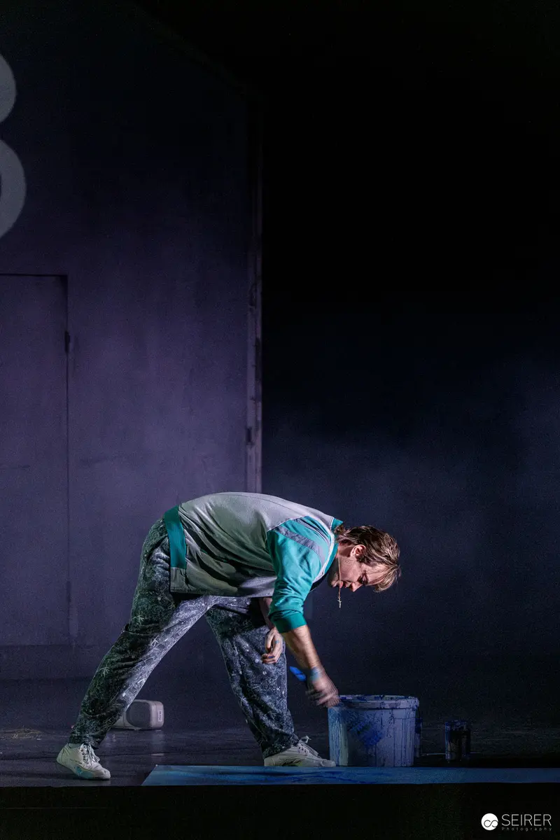 Actor in Green Bending Over Bucket During Theatrical Rehearsal of "Azur oder die Farbe von Wasser"