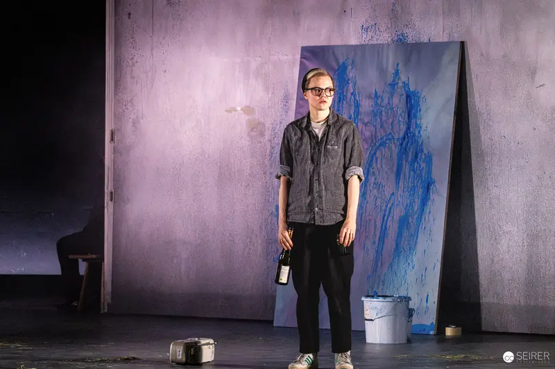 Artist Standing by Blue Splattered Canvas in Theater Staging