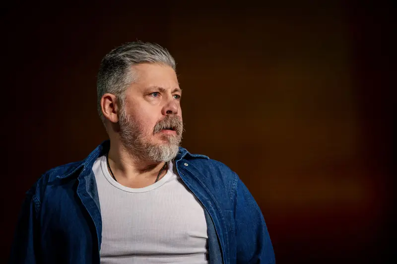 Contemplative Middle-Aged Man in Blue Denim Jacket Against Dark Background