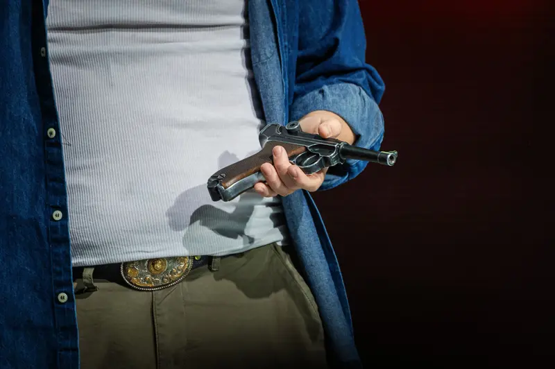 Man Holding Vintage Handgun in Blue Denim Jacket and Green Pants