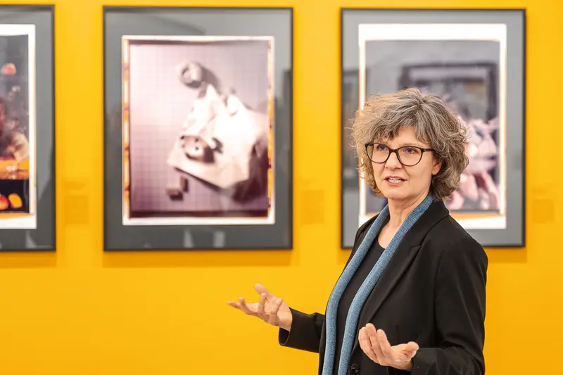 Curator Presenting Photography Exhibition Against Vibrant Yellow Wall