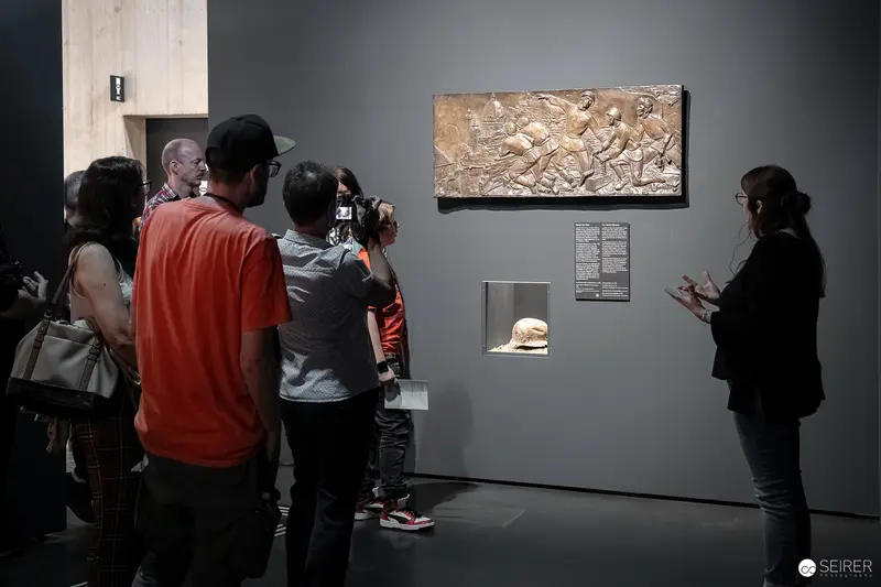 Exhibition Visitors Examining Historic Relief at Wien Museum Exhibit