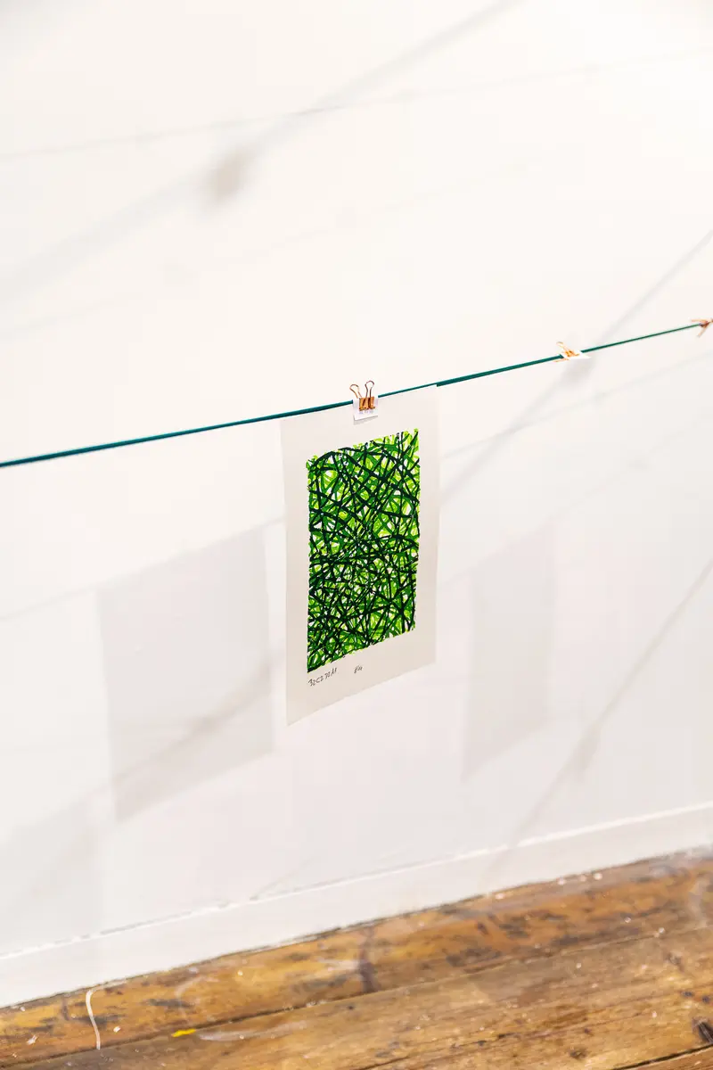 Green Rectangular Art Piece Hanging on Clothesline Against White Wall