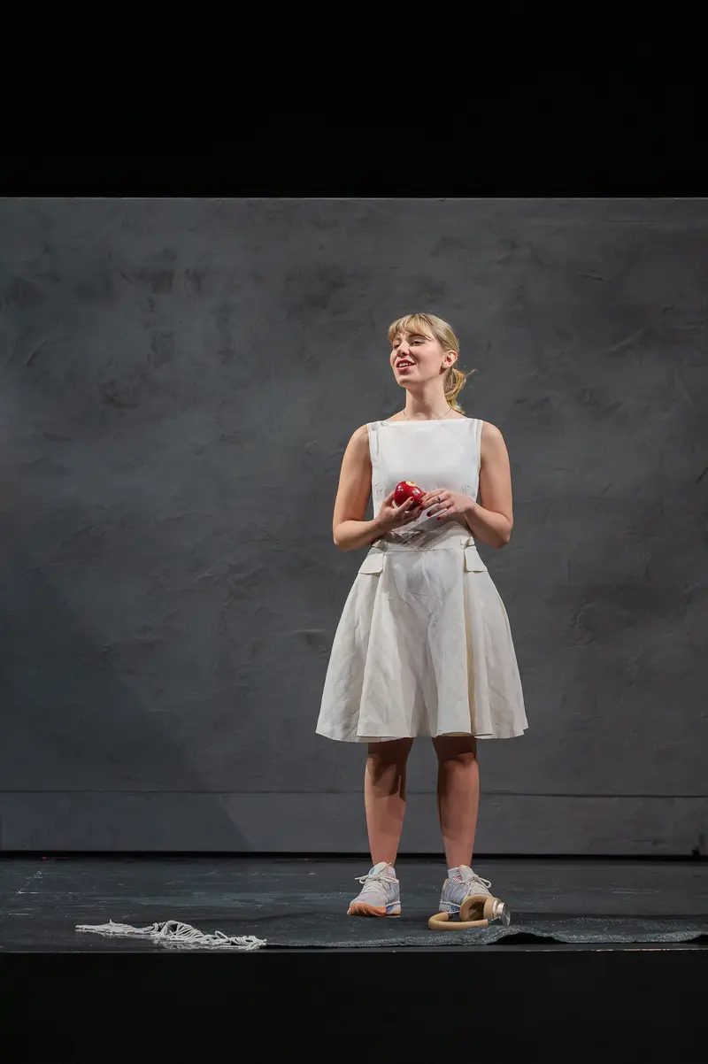 Performer in White Dress Holding Red Object During Theater Rehearsal