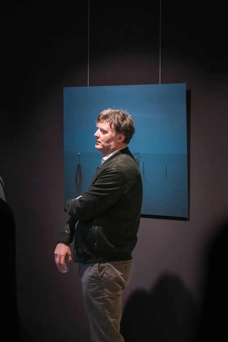 Art Gallery Vernissage: G. Herder Standing Before Blue Canvas at "Poem of Darkness" Exhibition
