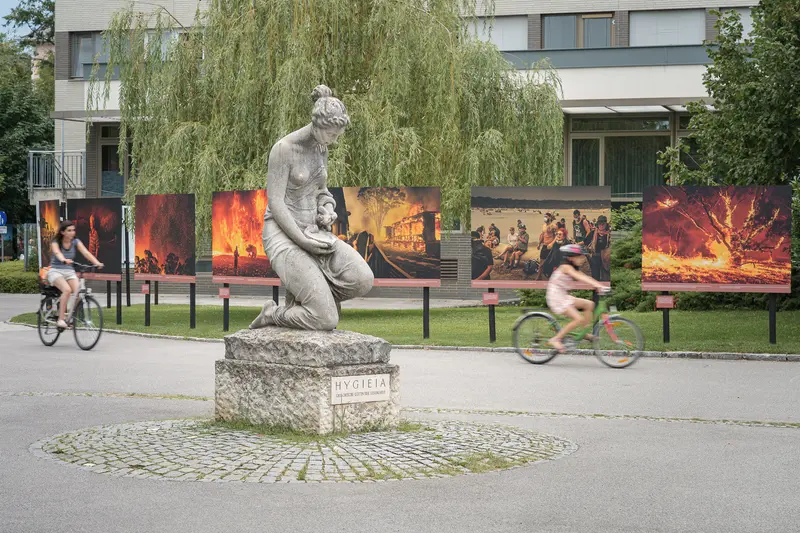Hygieia Statue Amid Fiery Photographic Exhibit in Urban Outdoor Setting