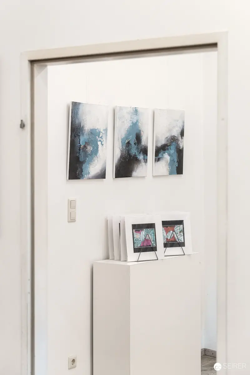 White Gallery Wall Displaying Blue-Toned Abstract Triptych and Framed Artwork