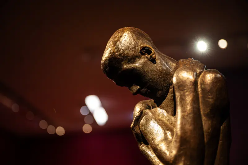 Bronze Sculpture of Contemplative Figure in Dark Exhibition Space