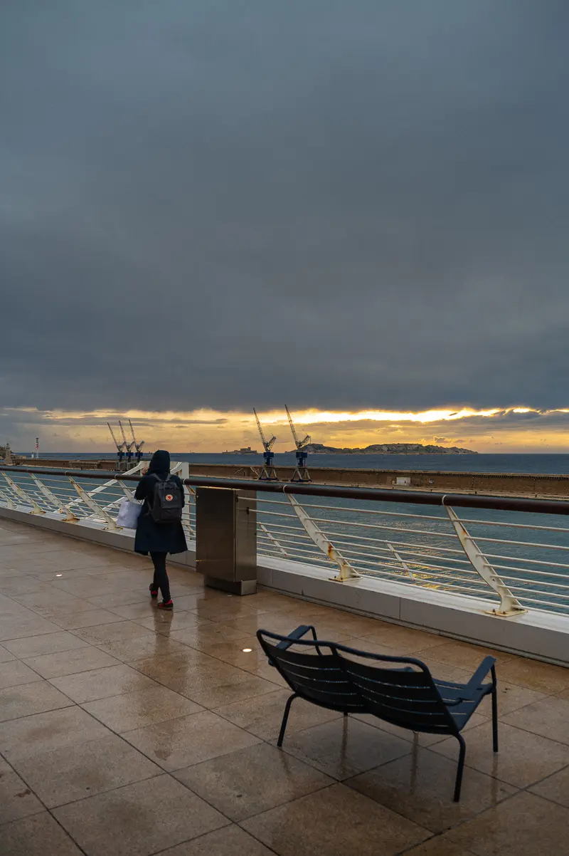 Solitary Figure Overlooking Harbor at Sunset in Cloudy Marseille