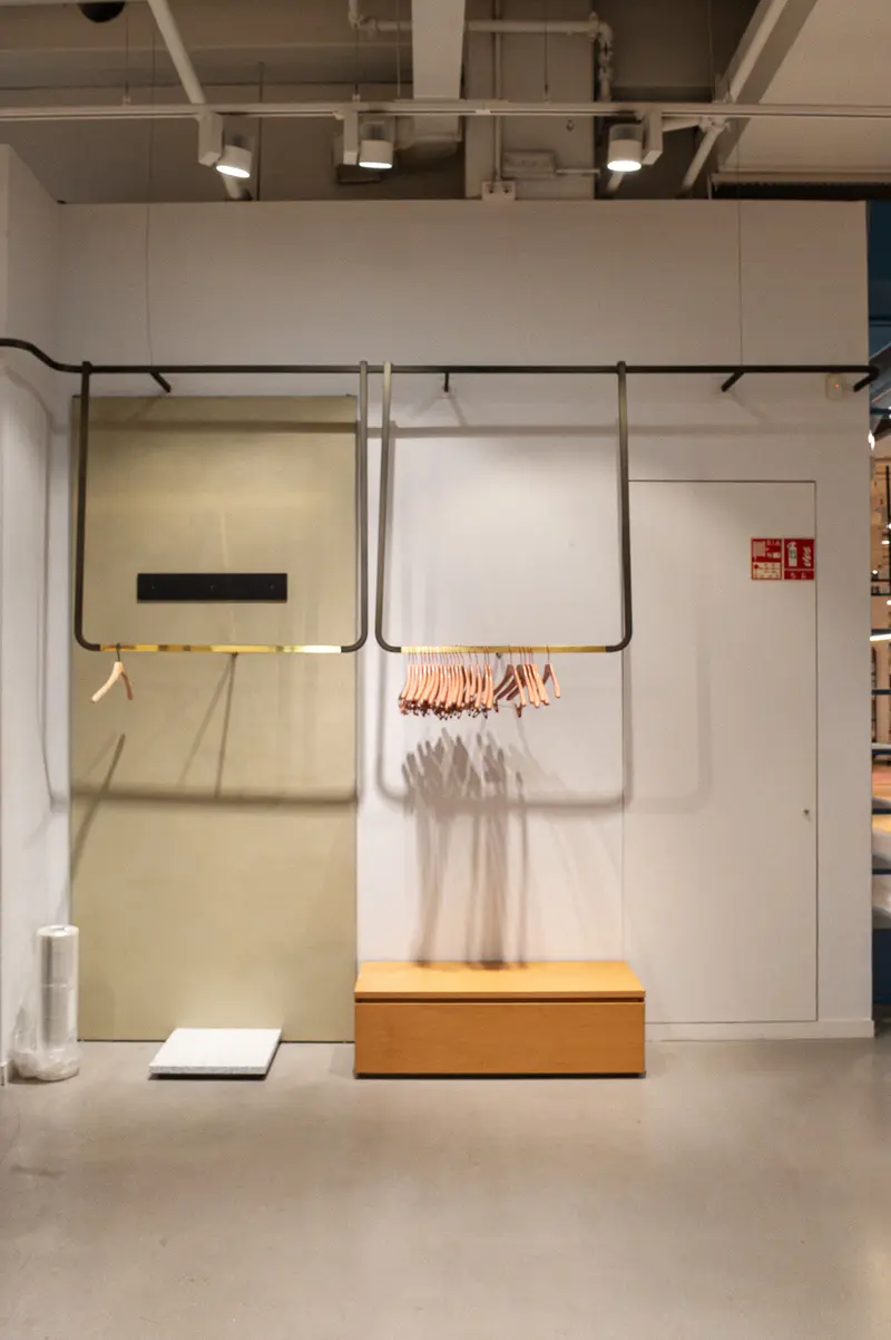 Minimalist Gallery Installation with Hanging Clothes and Wooden Bench