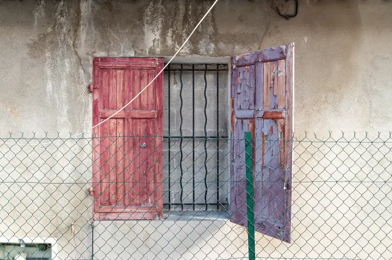 Weathered Red and Purple Doors Behind Chain-Link Fence in Aged Wall
