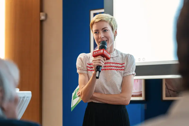 Short-Haired Speaker Addressing Event with Microphone in Blue-Walled Room