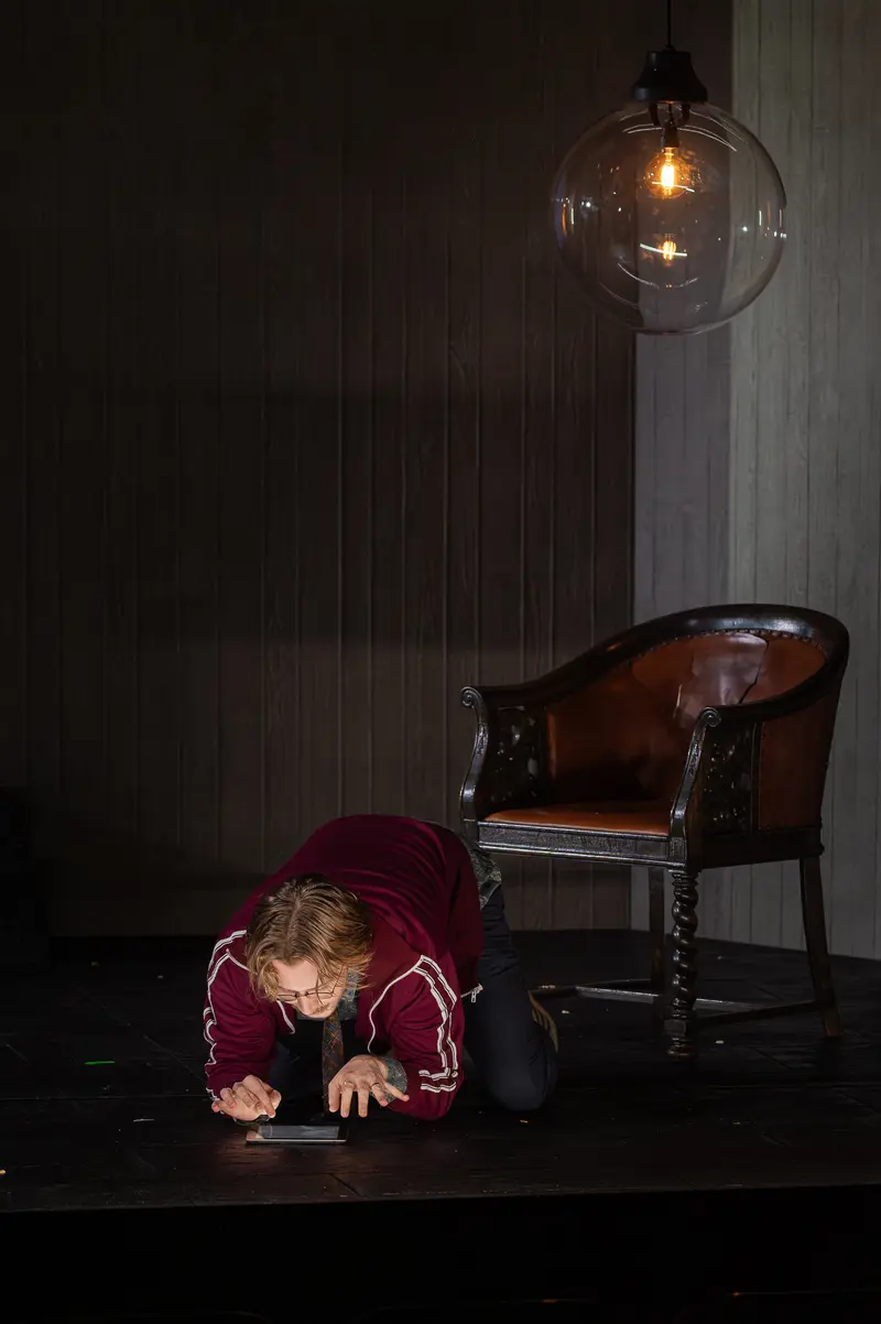 Actor in Burgundy Velvet Crouching on Darkened Stage