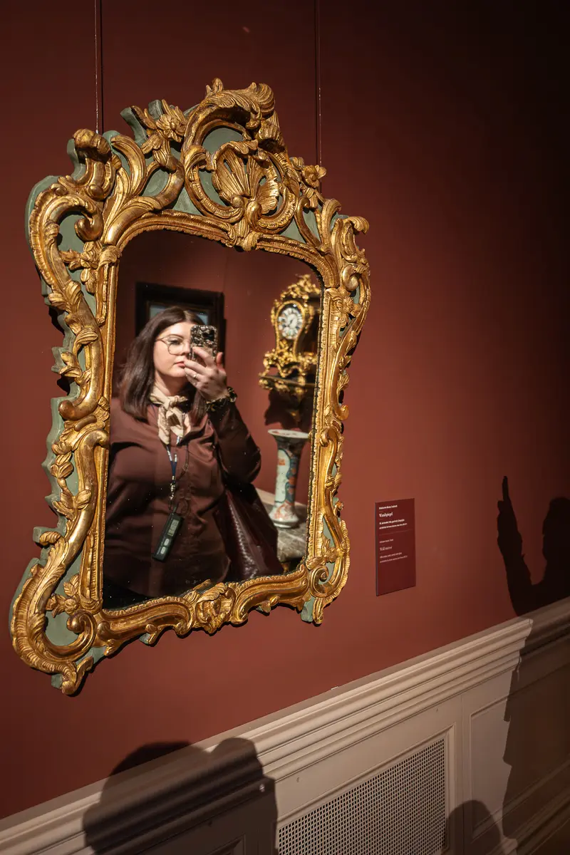 Person Posed in Ornate Golden Baroque Mirror Frame Against Burgundy Wall