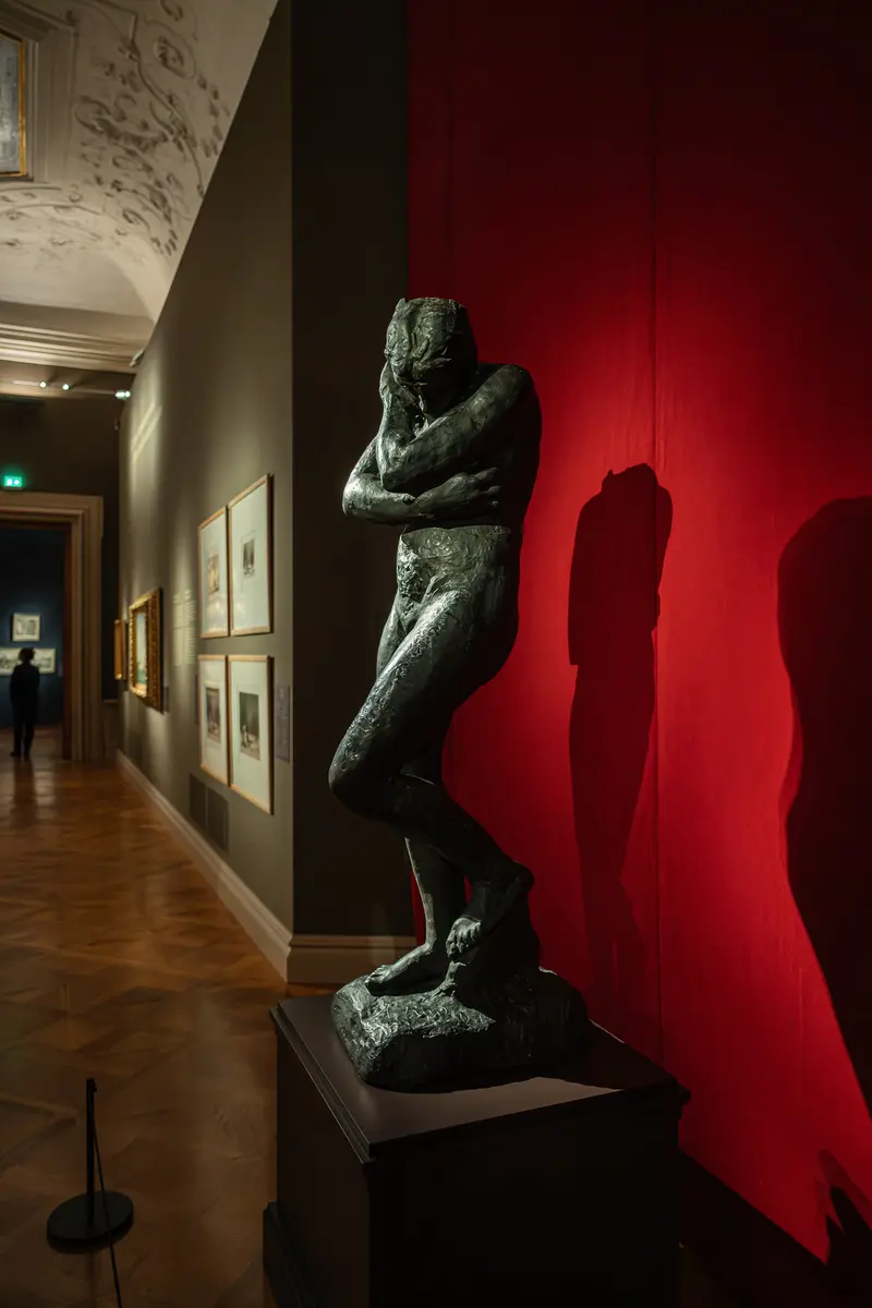 Bronze Sculpture of Male Figure Against Red Wall in Gallery