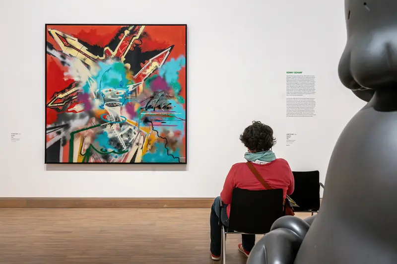Visitor views Kenny Scharf painting beside KAWS sculpture at Albertina Modern Vienna