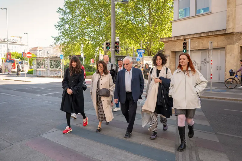 Group Walking Through Urban Street With Green Trees and Traffic Signals