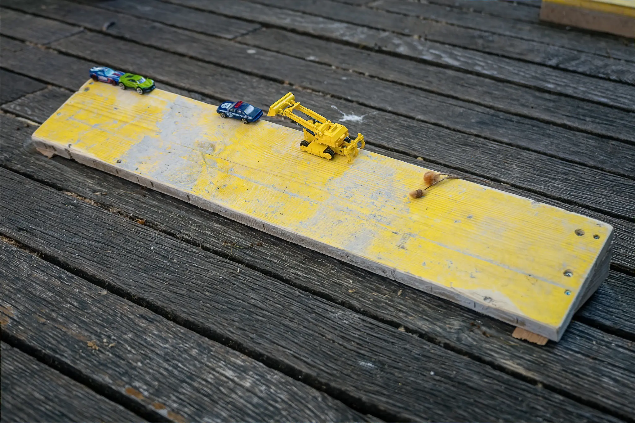 Toy Vehicles on Yellow Board Over Weathered Wooden Decking