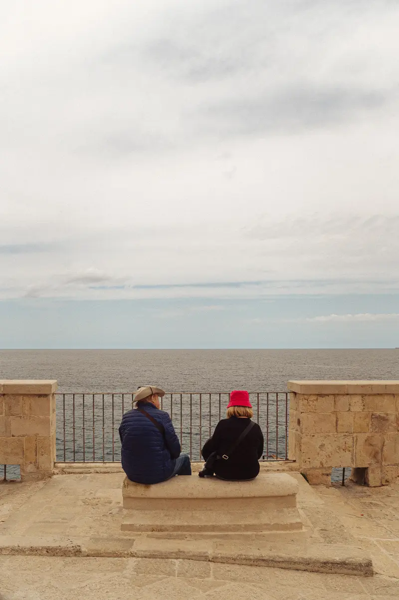 Two People Seated at Seaside Promenade Viewing the Ocean